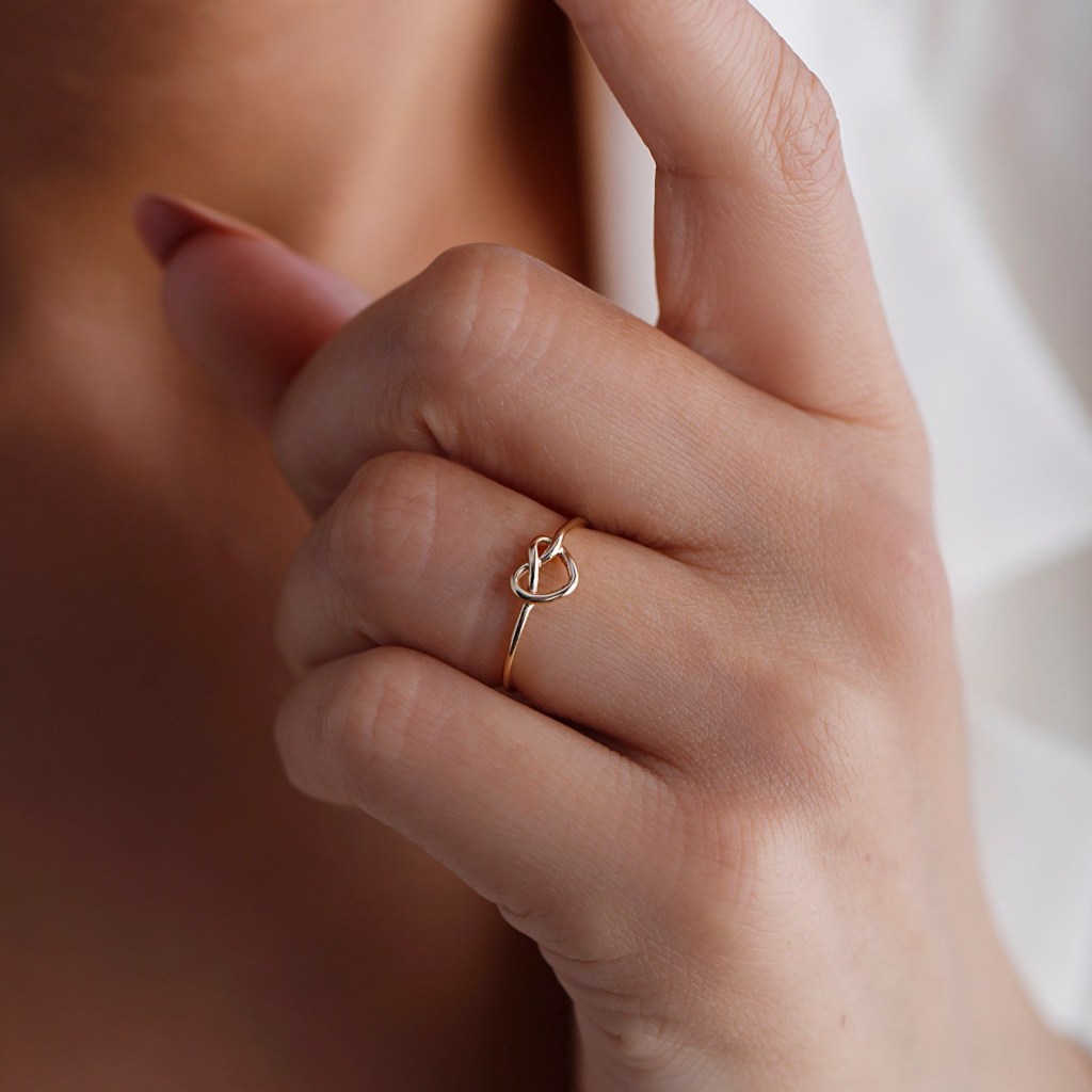 dainty gold promise ring with a heart knot design meaning eternal love and unity