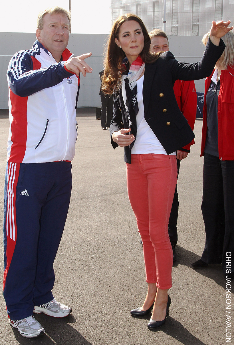 Kate Middleton pairs pink skinny jeans with navy heels, a navy blazer, a simple white tee and a neck scarf for a Team GB Olympics event. The Princess's look epitomises smart-casual