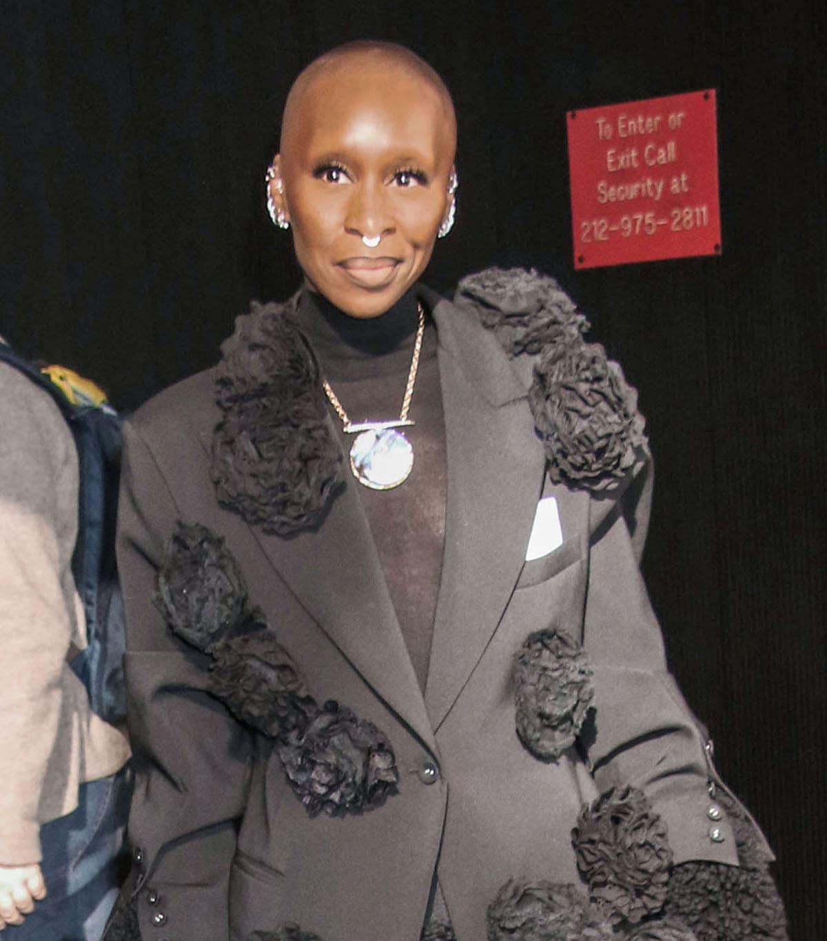 Cynthia Erivo adds glitz to her all-black ensemble with multiple earrings, rings, and a necklace with a mirror pendant