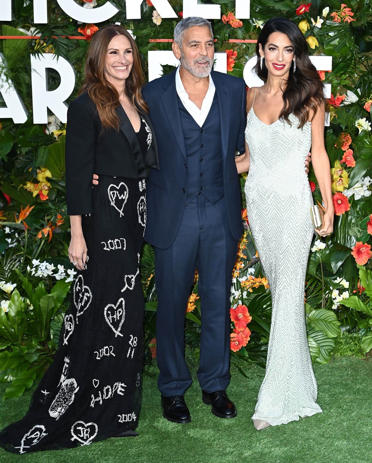 Julia Roberts stuns in a black Alexander McQueen gown with heart and hope embroidery, while George Clooney complements her with a sleek navy suit, and Amal Clooney dazzles in a shimmering white beaded gown