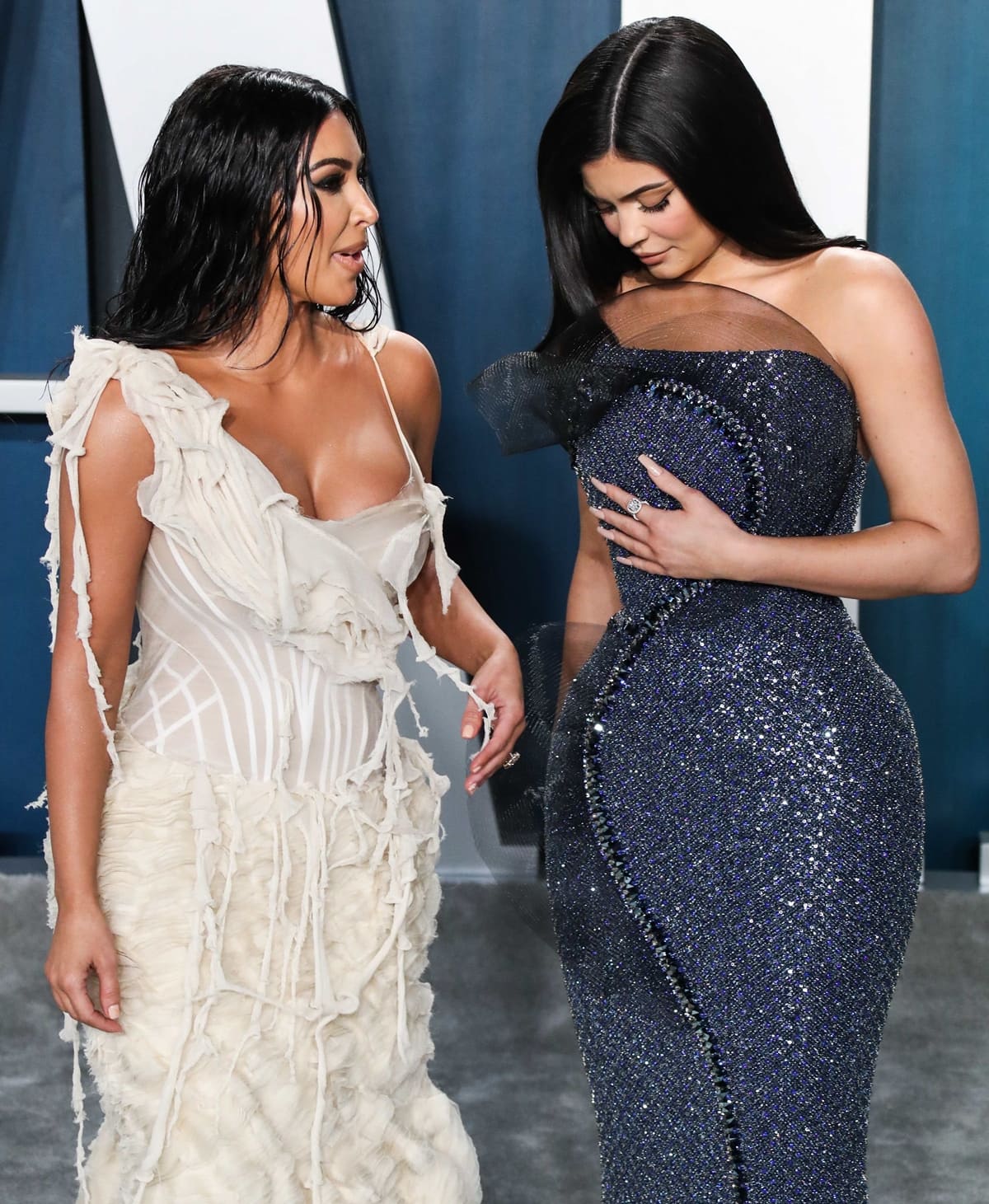 Kim Kardashian and Kylie Jenner attend the 2020 Vanity Fair Oscar Party, showcasing their distinct fashion choices with Kim in a white textured gown and Kylie in a glittering navy dress