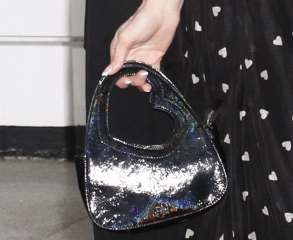 Paris Hilton enhances her dress's romantic vibe by carrying a black iridescent bag featuring a heart-shaped handle from her Walmart bag collection